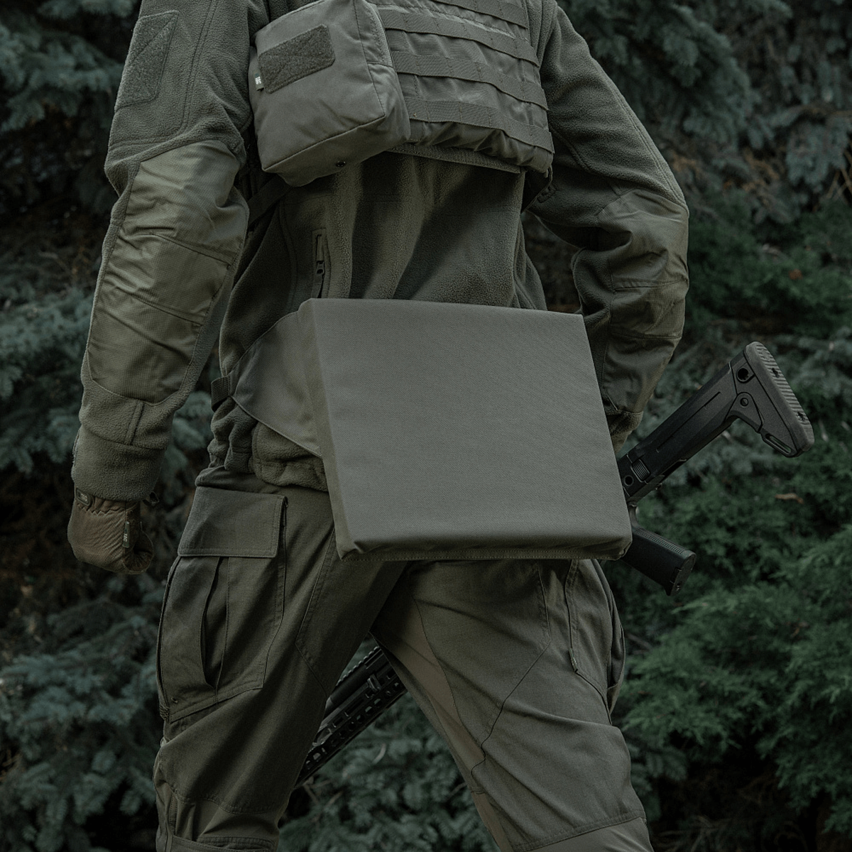 M-Tac Siddeunderlag med bælte båret af person i naturmiljø, til praktisk udendørs siddekomfort