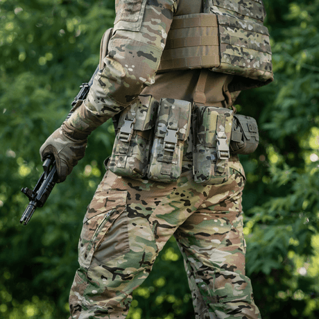 Man i camouflagedräkt med M-Tac dubbel magasinficka med Fastex-låsning, redo för militära och säkerhetsuppdrag i skogen