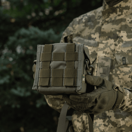 M-Tac Taske til Natkikkert PVS-14 holdt af en person iført kamouflageudstyr i skovbaggrund, designet til sikker opbevaring af natkikkerter.