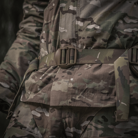 Närbild av militär uniform med kamouflagemönster, fokus på bälteområdet i skogsmiljö.