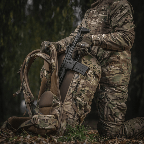 Person i kamouflage håller vapen och M-Tac Ryggsäck Large Gen.IV Elite i skogsområde.