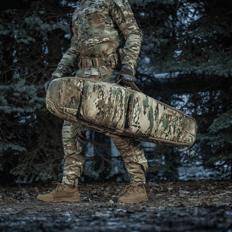 Soldat bär M-Tac Gun Backpack Case 125 cm Gen.II Elite i en skog, iförd camouflageuniform