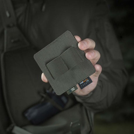 Person håller M-Tac Double Mag Pouch Hook Backed Magazine framför en mörk bakgrund