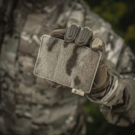 M-Tac panel för patches på MOLLE 120x85 i camouflagemönster, hålls av person i taktisk utrustning, med hook & loop-yta