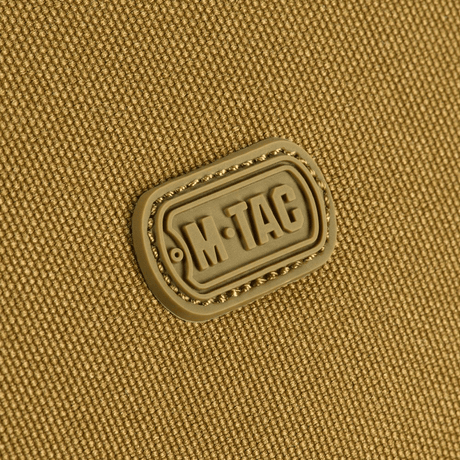 Close-up af M-Tac Toilettaske logo på slidstærkt 600D polyester med PVC-belægning, perfekt til kompakt opbevaring og rejsebrug.