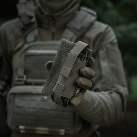 M-Tac Tourniquet Pouch Elastisk VELCRO Gen.II hålls av en person i taktisk utrustning för snabb åtkomst till tourniquet