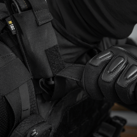 Person i svart skyddsutrustning använder M-Tac Tourniquet Pouch Elastisk med MOLLE Gen.II fäst vid västen.