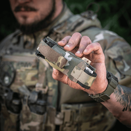 M-Tac Tourniquet Pouch Elastisk med MOLLE Gen.II i kamouflage, hålls av person i militäruniform, snabb åtkomstficka för tourniquet.