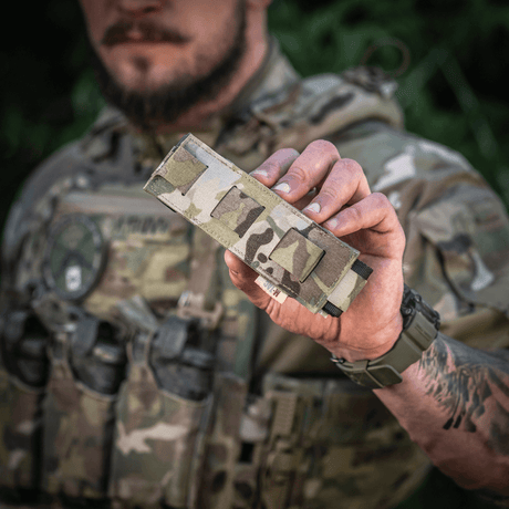 M-Tac Tourniquet Pouch Elastisk med MOLLE Gen.II i camo-design hålls av person med taktisk utrustning, visar enkel åtkomst och förvaring.