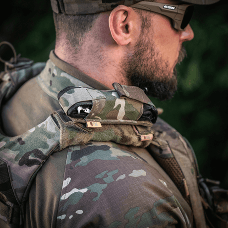 M-Tac Tourniquet Pouch Elastisk med MOLLE Gen.II på axeln av en taktiskt klädd man utomhus, snabb åtkomst och säkerhet.