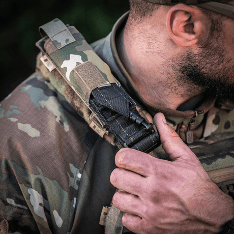 M-Tac Tourniquet Pouch Elastisk med MOLLE Gen.II fäst på axeln av en taktisk väst, visar snabb åtkomst och hållbarhet.