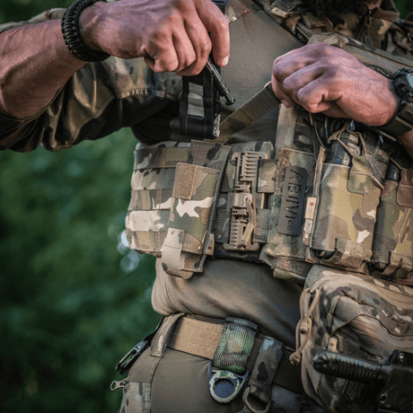 Soldat bär M-Tac Tourniquet Pouch Elastisk med MOLLE Gen.II på militärutrustning i naturmiljö.