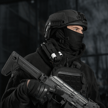Taktisk person i svart utrustning och hjälm med vapen och utrustning, redo för uppdrag.