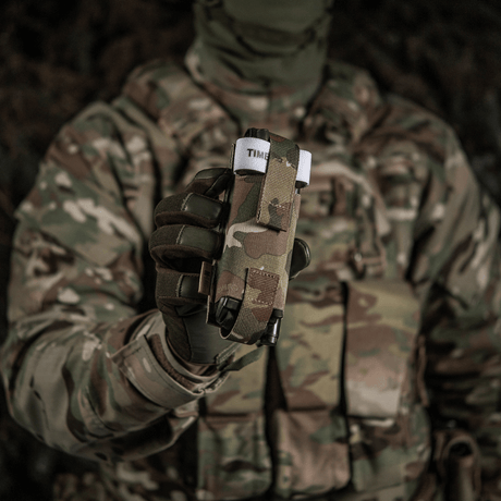 Soldat i kamouflageuniform håller M-Tac elastisk tourniquetficka Molle Gen.III framme, redo för snabb åtkomst.