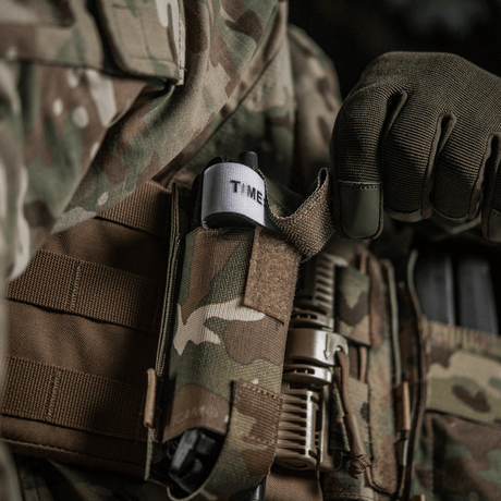 M-Tac elastisk tourniquetficka Molle Gen.III i kamouflage, fäst på taktisk väst med tourniquet synlig.