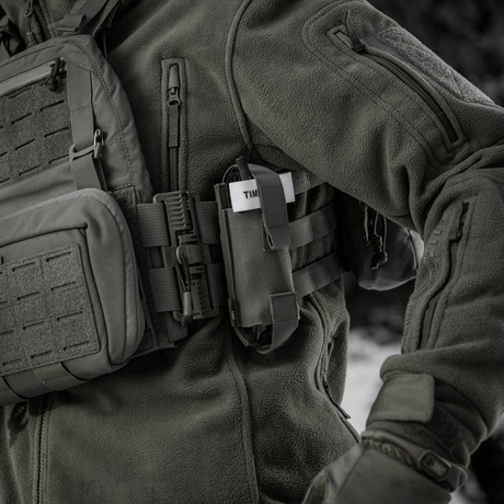 M-Tac elastisk tourniquetficka Molle Gen.III fäst vid taktisk jacka på person i fältet.