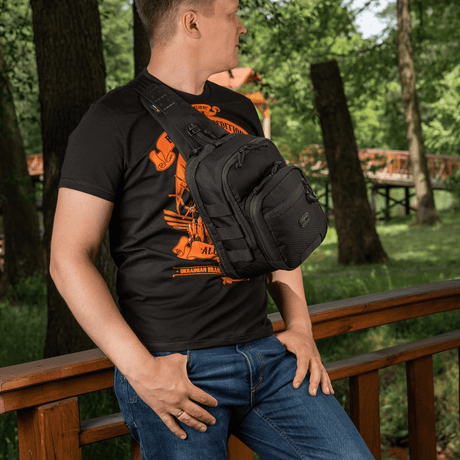 Man bär M‑Tac Cross Bag Elite Hex på en bro i skogen, perfekt för dagligt bruk. Väskan rymmer upp till 5 liter.