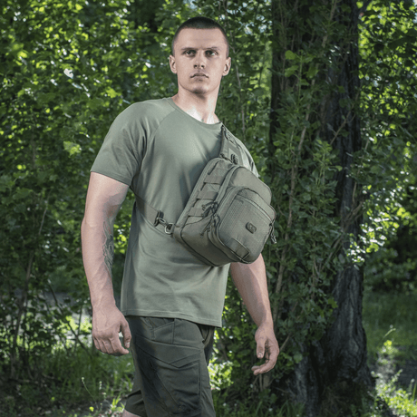 Man bär M‑Tac Cross Bag Elite Hex i skogsmiljö, idealisk för vardagsbruk och taktisk utrustning.