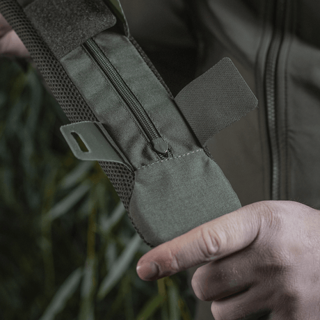Person håller M‑Tac axelremspad 50 mm Elite i robust Cordura-material med dragkedjeförslutning och 3D-mesh för ventilation.