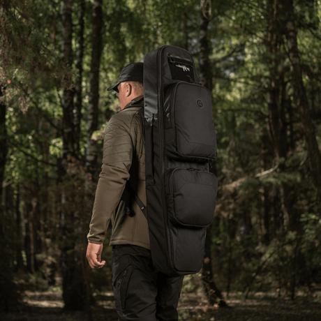Man bär M-Tac Gun Backpack Case 105 cm Elite Hex genom skogen, idealisk för AR-15 och AK karbiner-transport. Cordura 500D-material.