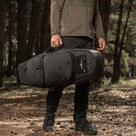 Man bär M-Tac Gun Backpack Case 105 cm Elite Hex i skogen, idealisk för jakt och skytte, designad för AR-15 och AK karbiner.