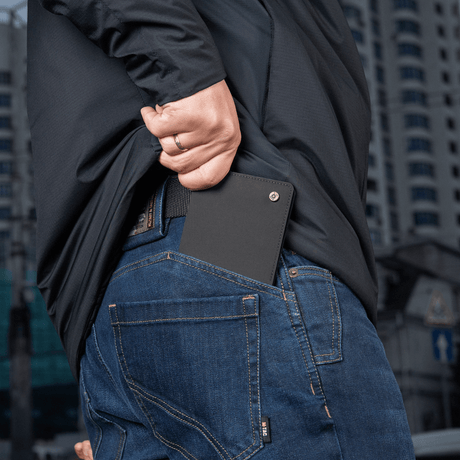 Person stoppar M‑Tac Pung Slim Elite i bakfickan på jeans, kompakt och stilfull design för kort och kontanter.