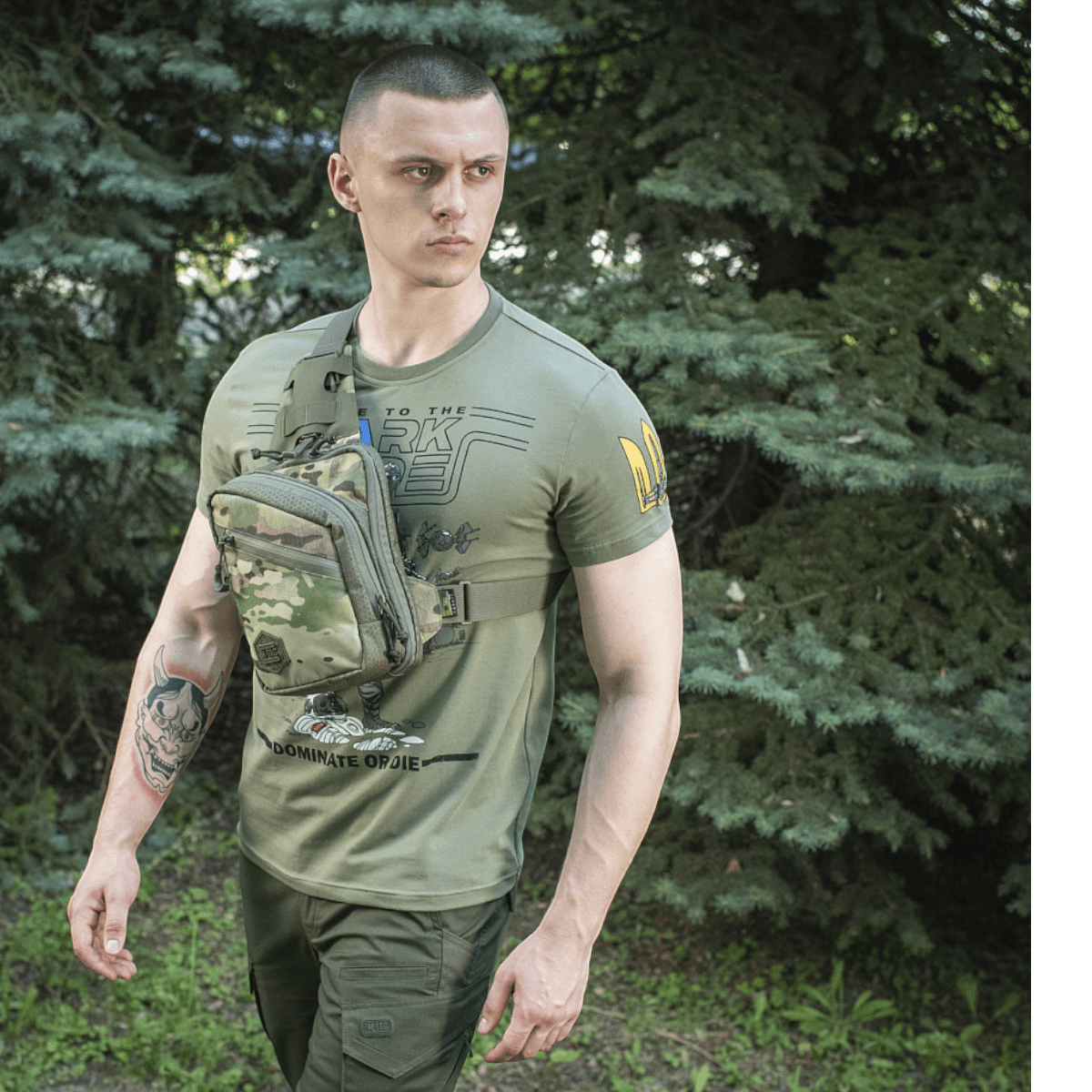 Mand med grøn M-Tac Sling Pistoltaske Elite Hex, lavet af robust Cordura, med justerbar rem i skovområde.