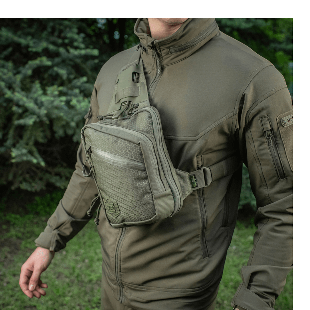 Mand bærer M-Tac Sling Pistoltaske Elite Hex over brystet i skovmiljø, lavet af robuste materialer som Cordura 1000D og Cordura Hex.