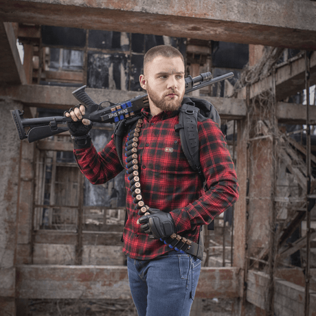 Man bär M-Tac Bandolier Elite och skjutvapen i industriell miljö, designad för snabb åtkomst till ammunition.