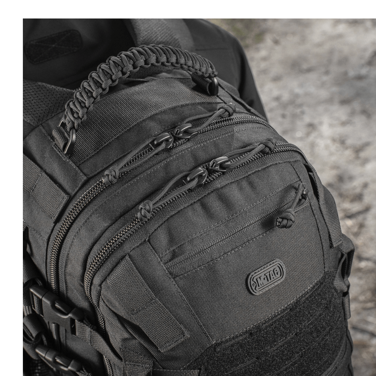 Nærbillede af M-Tac Mission Pack Elite rygsæk i slidstærk Cordura 1000D, med MOLLE LASER CUT-system i sort design på ujævn terræn.
