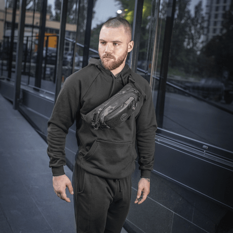 Man i svart klädsel bär M‑Tac bältesväska Elite Hex utomhus. Kompakt och stilren väska idealisk för vardagligt bruk och taktisk utrustning.