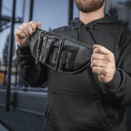 Man håller M‑Tac bältesväska Elite Hex, kompakt och funktionell i Cordura-tyg med YKK-dragkedjor, perfekt för taktisk utrustning.