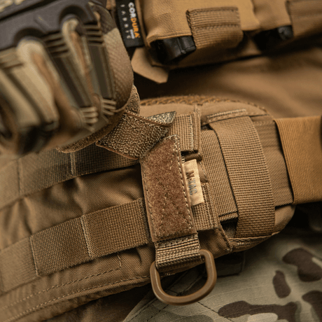 M-Tac fäste med D-ring för MOLLE-system på taktisk utrustning, med Velcro-justering. Kompakt och lätt design för taktisk användning.