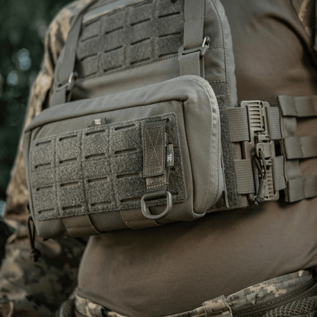 M-Tac fäste med D-ring monterat på taktisk väst med MOLLE-system för säker upphängning av utrustning via Velcro-låsning.