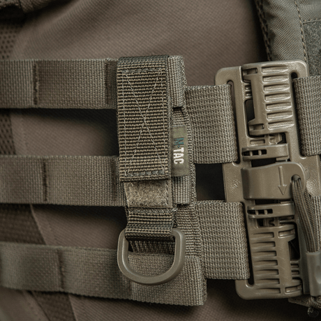 M-Tac fäste med D-ring monterat på MOLLE-system med Velcro-låsning, idealisk för taktisk användning och lätt justerbar.