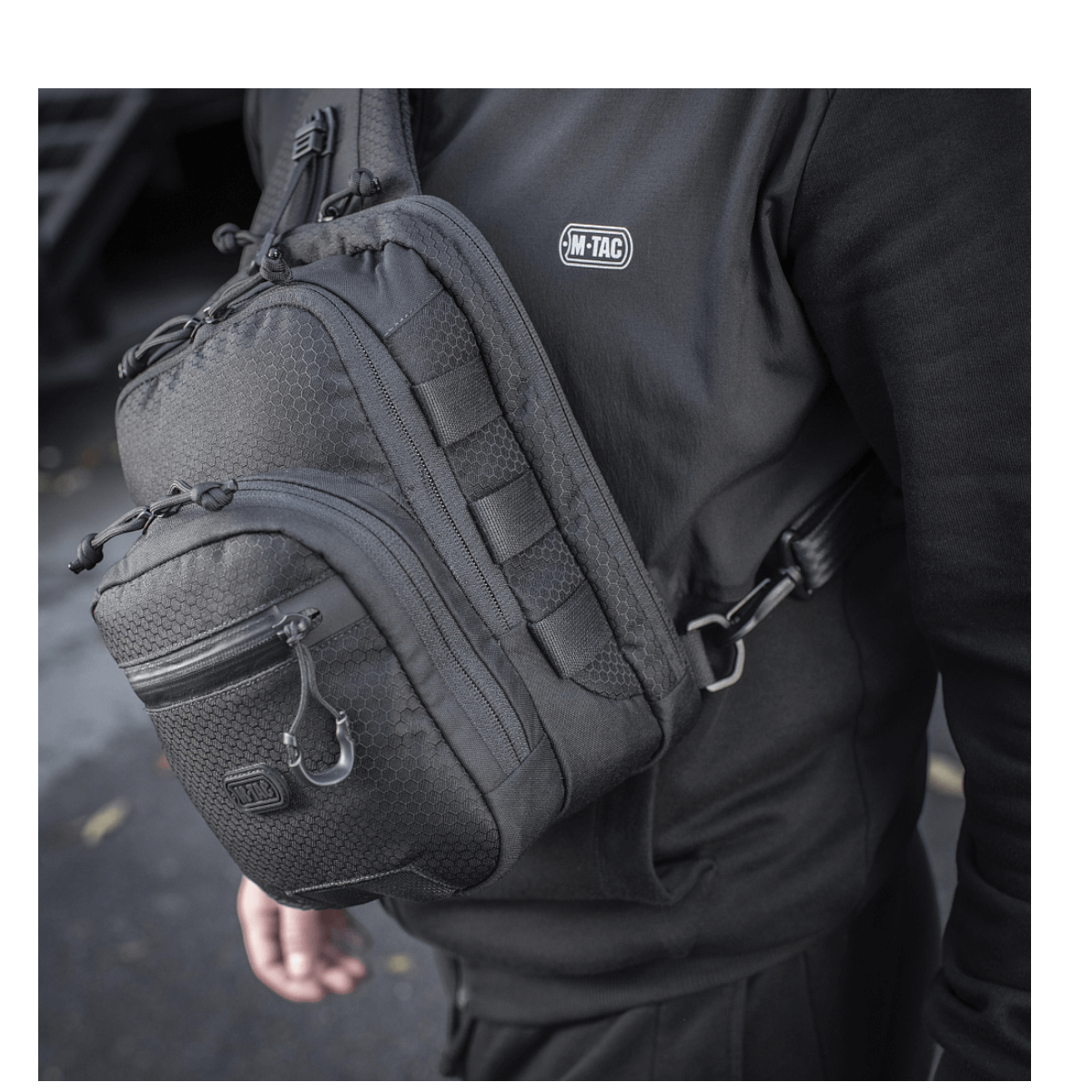 Person med M-Tac Cross Taske Slim Elite Hex lavet af Cordura 500, sort design, justerbar rem, YKK lynlåse. Ideel til hverdagsbrug.