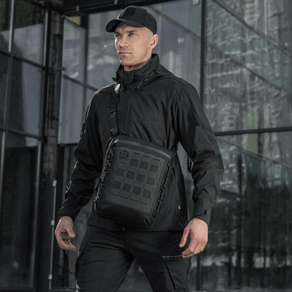 Mand med M-Tac Tablet Bag Laser Cut Hex i sort, ideel til EDC, dokumenter og tablet, fremstillet i holdbart Cordura-materiale.