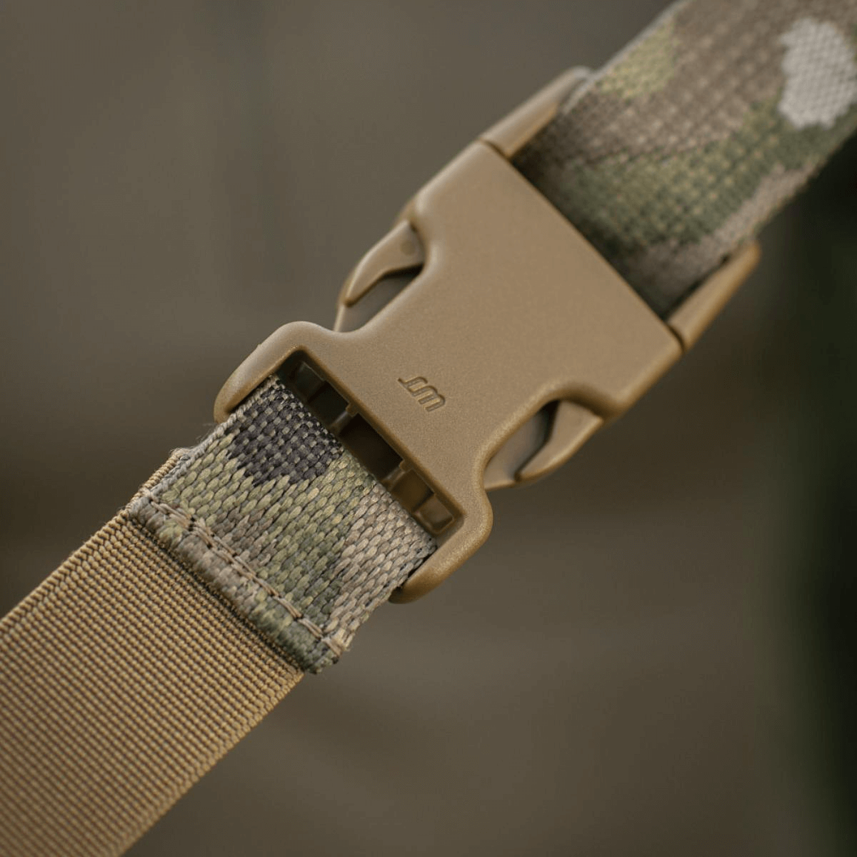 Nærbillede af en kamufleret plastikspænde på en strop, brugt i friluftsudstyr.