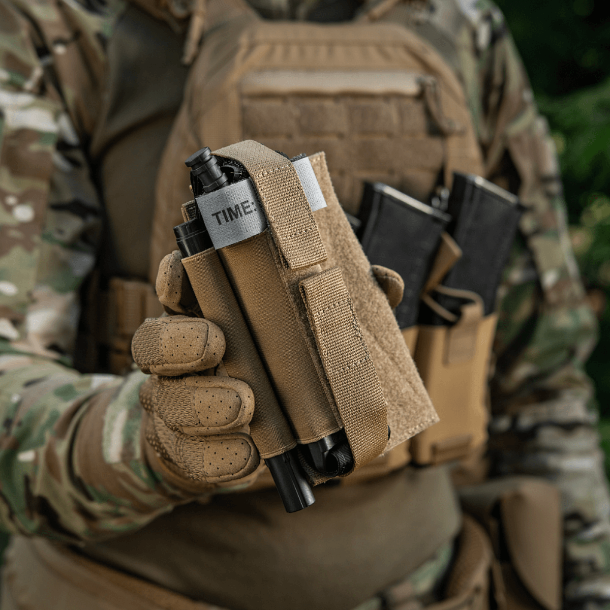 Taktisk udstyr med M‑Tac Tourniquet Pouch Elastic Gen.5 monteret på vest, holdende en tourniquet i naturmiljø på en soldat.