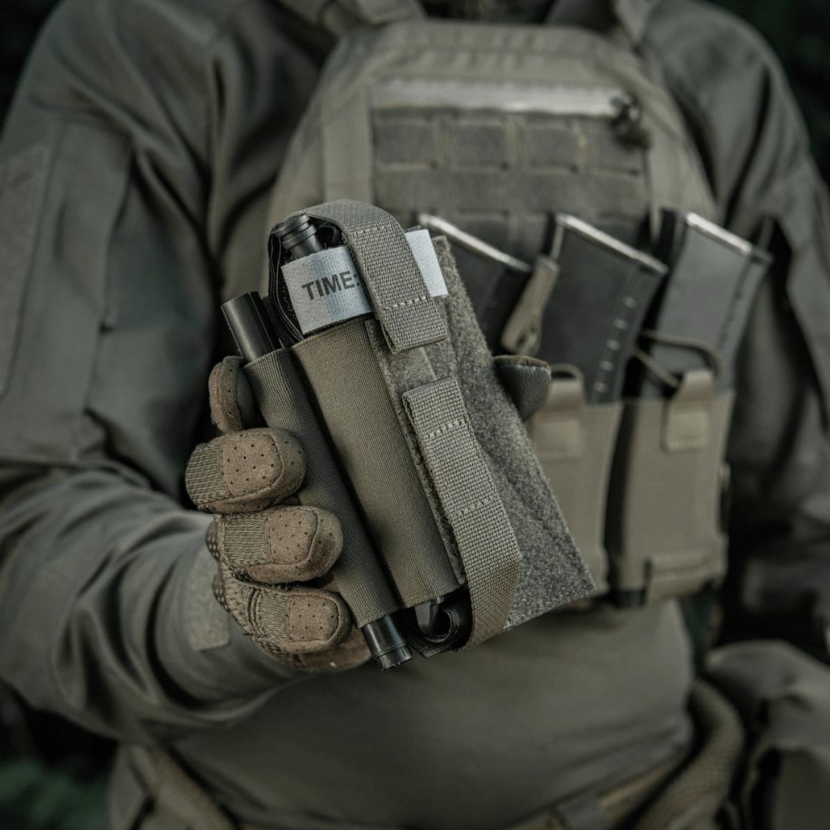 M‑Tac Tourniquet Pouch Elastic Gen.5 fastgjort til taktisk udstyr med CAT tourniquet og magasinhylster i baggrunden
