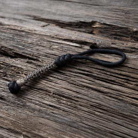 M‑Tac Knife Lanyard Scandinavian i flätad paracord, stilfullt och praktiskt tillbehör för fickknivar på träbakgrund.