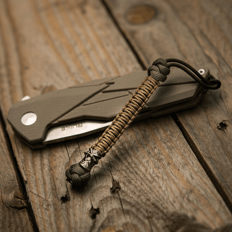 M-Tac Knife Lanyard Ninja i paracord bredvid fällkniv på träbord