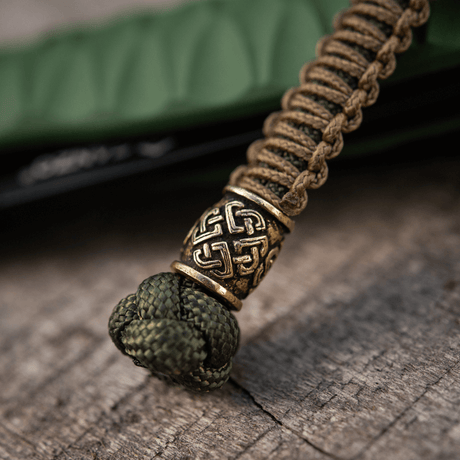 M-Tac Knife Lanyard Celtic i flätad paracord med keltiskt mönster, knivtillbehör på träliknande yta.