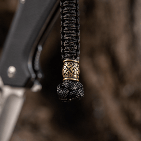 M-Tac Knife Lanyard Celtic i flätad paracord med dekorativt mönster, visad på en kniv som ett stilfullt och praktiskt tillbehör.
