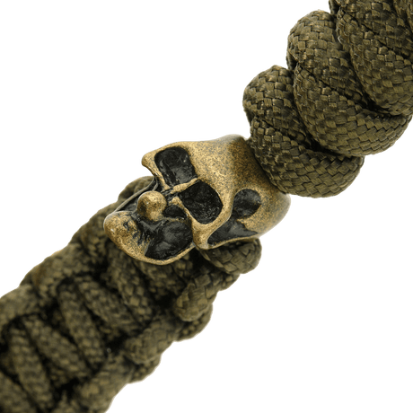 Detalj av olivgrön M-Tac Loopy Snake Skull Lanyard, visad med flätad paracord och dekorativ metallskalle, för kniv och utrustning.