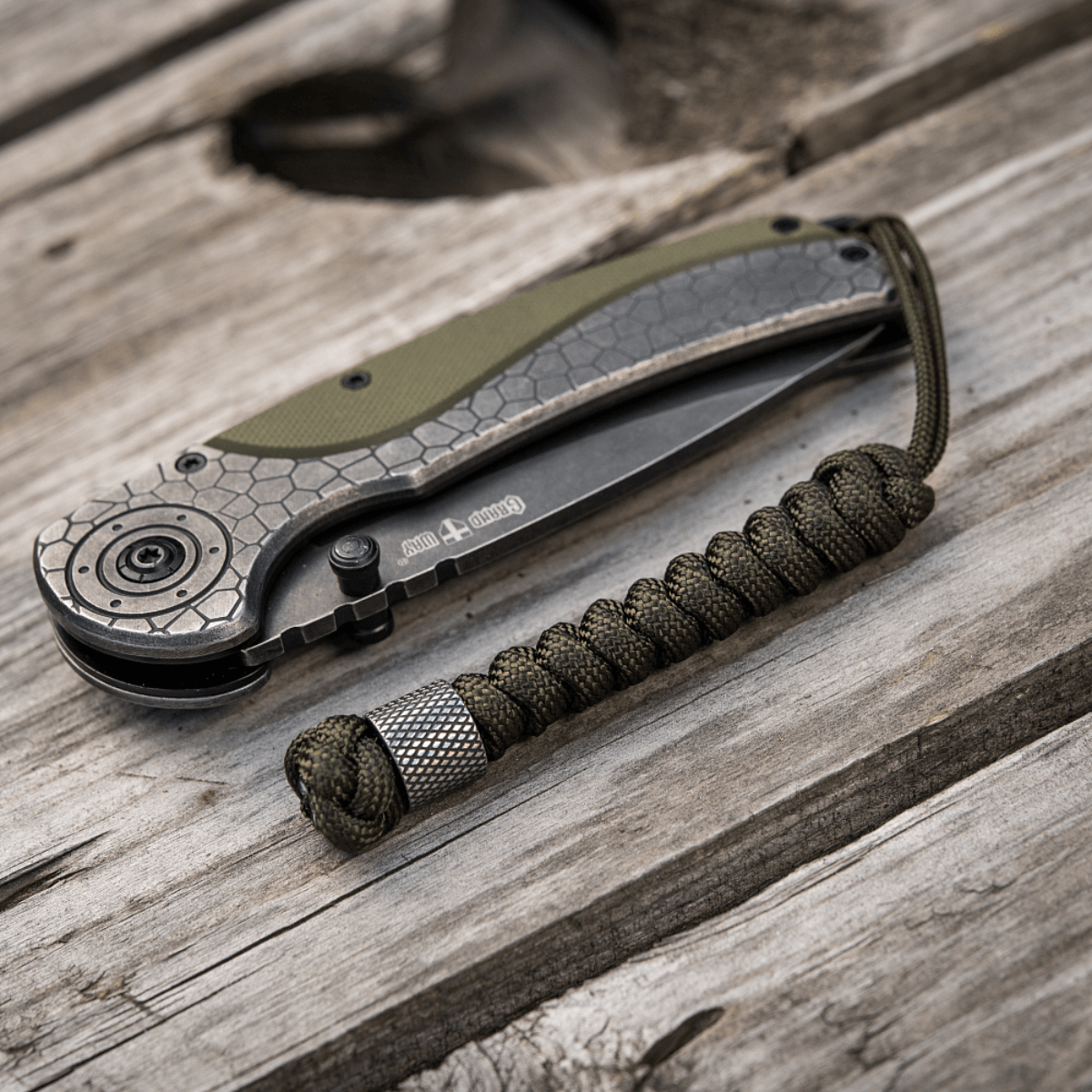 M-Tac Viper Lanyard Stainless Steel i flettet paracord ved siden af en sammenklappelig kniv på et træbord.