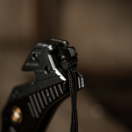 Detaljbild av M-Tac Zeus Lanyard, flätad med paracord för snabb åtkomst och stilfull design, fäst vid knivhandtag.