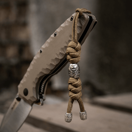 M-Tac Zeus Stainless Steel Lanyard med flätad paracord och dekorativa pärlor på en kniv, används för snabb åtkomst till utrustning.