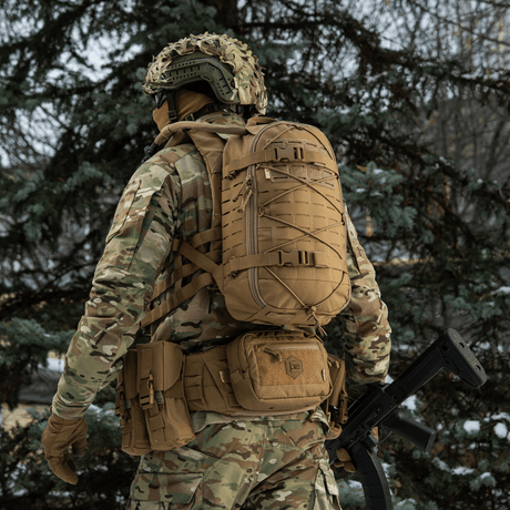 M-Tac Rygsäck Sturm Elite Gen.II i fältet, person i camouflagedräkt och taktisk ryggsäck med MOLLE-system och förstärkta remmar, skogsmiljö.