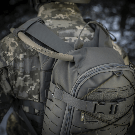 M-Tac Ryggsäck Sturm Elite Gen.II i grått Cordura-tyg på soldat i kamouflage, visar inbyggt vätskesystem med slang i naturen.
